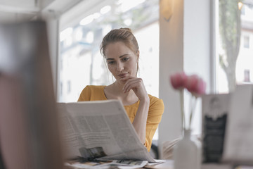 Young woman sitting in coworking space, reading newspaper