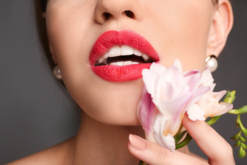 Beautiful young woman with bright red lipstick and flower on grey background, closeup