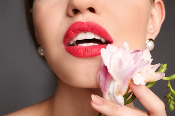Fototapeta na wymiar Beautiful young woman with bright red lipstick and flower on grey background, closeup