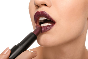 Beautiful young woman applying dark lipstick on white background, closeup