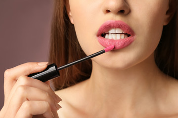 Fototapeta premium Beautiful young woman applying pink lipstick on color background, closeup