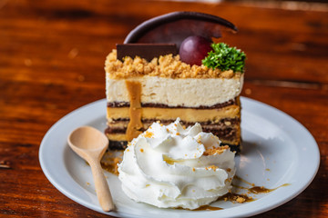 Chocolate cake and cream in white plate on wooden table.