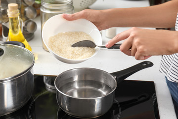 Woman pouring raw rice into saucepan with boiling water on stove