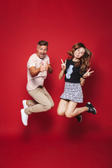 Full length photo of excited man and woman in striped t-shirt jumping, while showing victory sign,...