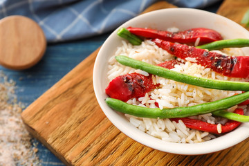 Plate with tasty boiled rice and vegetables on wooden board