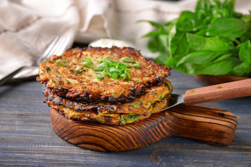 Wooden board with zucchini pancakes on table