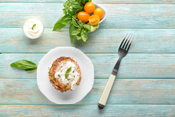 Plate with zucchini pancakes and sauce on wooden table