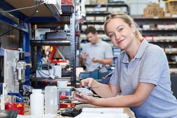 Portrait Of Female Engineer In Factory Measuring Component At Work Bench Using Micrometer