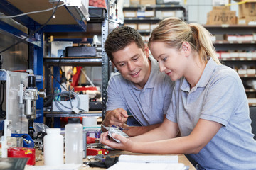 Engineer Helping Female Apprentice In Factory To Measure Component Using Micrometer