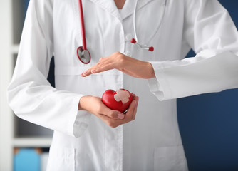 Cardiologist holding red heart with plaster in clinic, closeup