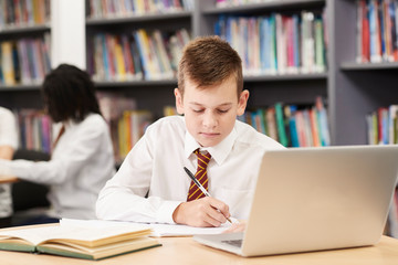Male High School Student Wearing Uniform Working At Laptop In Library