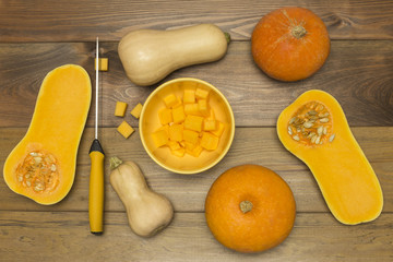 Pumpkin slices in yellow glass bowl with pumpkins near and knife at wooden background