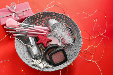Wicker bowl with cosmetics and Christmas present on color background