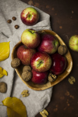 Composition with pink lady apples, walnut, hazelnut and leafs at beige napkin on brown background