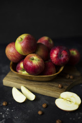 Pink lady apples in wooden bowl on wood board at black background