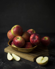 Pink lady apples in wooden bowl on wood board at black background