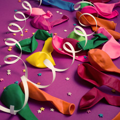 Festive background of purple material colorful balloons streamers confetti Top view flat lay