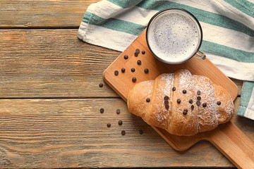 Tasty croissant with cup of beverage on wooden background