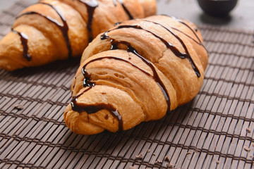 Tasty croissants with chocolate syrup on bamboo mat