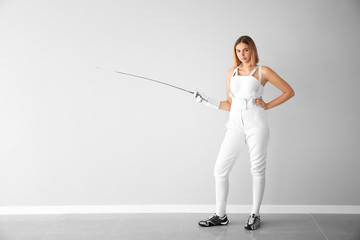Young female fencer near light wall