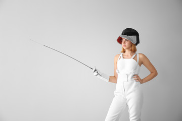 Young female fencer on light background