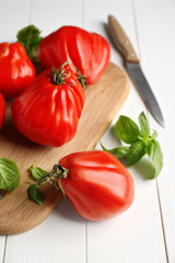 Board with delicious tomatoes and fresh basil on white wooden table