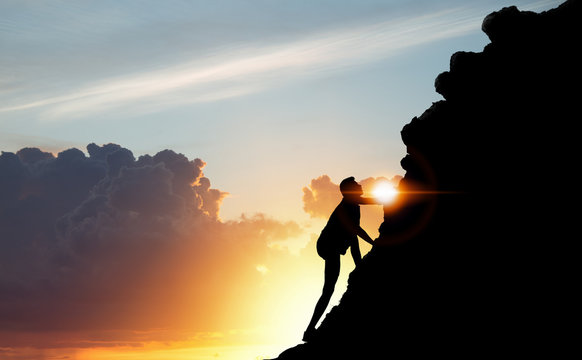 A silhouette of man climbing on mountain top over sunset background, Business, success, leadership, achievement, attempt, patient, endeavor and people concept.