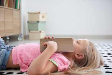 Cute little girl sleeping with book on floor at home