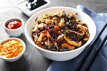 Bowl with boiled rice and seafood on grey table