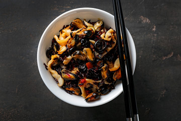 Bowl with boiled rice and seafood on dark table