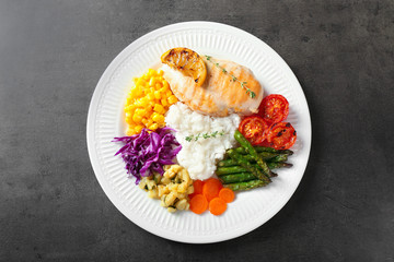 Plate with boiled rice, vegetables and meat on dark table