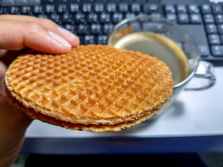 Man picks up stroopwafel to eat in front of woking table. Stroopwafel a famous waffle from dutch. Eat it with black coffee.
