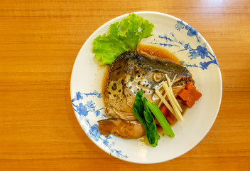 Delicious Salmon head boiled in Soy sauce served on Japanese style dish garnished with mixed vegetables put on the wooden table.