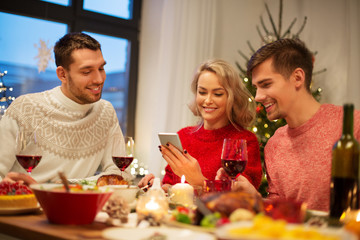 holidays and celebration concept - happy friends with smartphone having christmas dinner at home