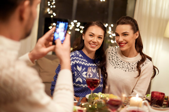 holidays and celebration concept - happy friends having christmas dinner at home and taking picture by smartphone