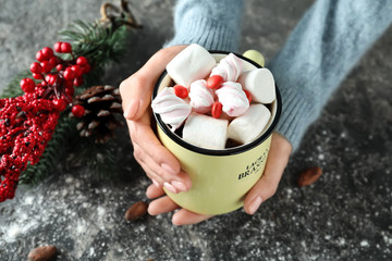 Woman with cup of tasty cocoa and marshmallows at grunge table, closeup
