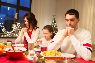 holidays, family and celebration concept - happy mother, father and little daughter having christmas dinner and praying before meal at home
