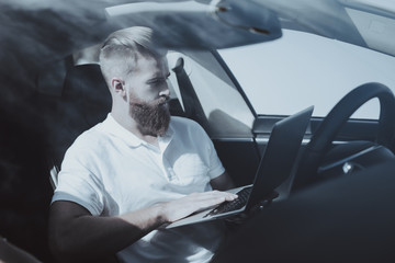 Fototapeta na wymiar Man Works With Laptop In Front Seat Of Tesla Car.