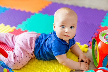 Portrait of cute baby boy lying on floor covered with multicolored soft mats in playroom. Adorable toddler kid smiling and playing with colorful toys indoor. Chilld growing and development