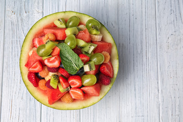 Delicious fruit salad in watermelon bowl on light wooden table