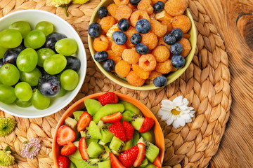 Fototapeta na wymiar Delicious fruit salads in bowls on wicker mat