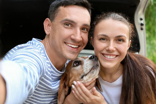 Young couple with cute dog taking selfie near car outdoors