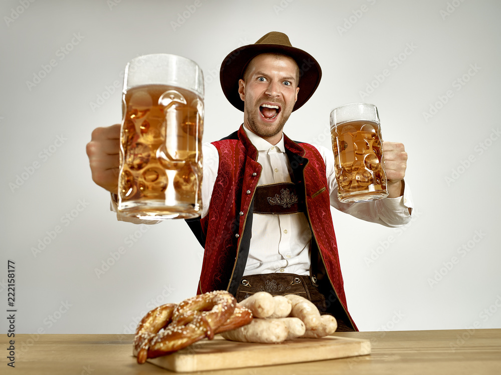 Wall mural Germany, Bavaria, Upper Bavaria. The young happy smiling man with beer dressed in traditional Austrian or Bavarian costume holding mug of beer at pub or studio. The celebration, oktoberfest, festival