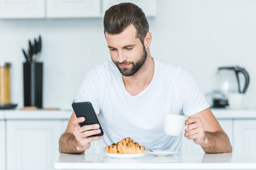handsome bearded young man using smartphone during breakfast