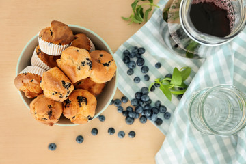 Bowl with tasty blueberry muffins and jug of juice on wooden table