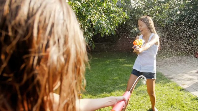 Slow mtoion footag eof two teenage girls playing with water guns on grass at backyard