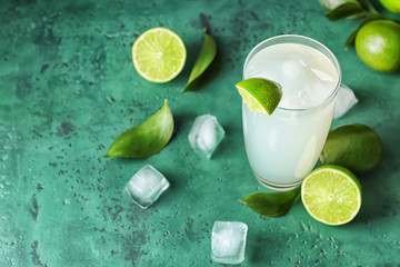 Glass of fresh lime lemonade on color table