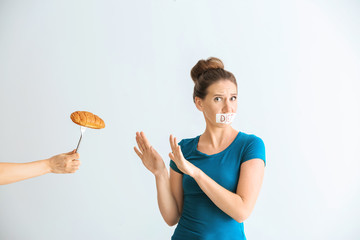 Woman with taped mouth refusing to eat unhealthy food on white background. Diet concept