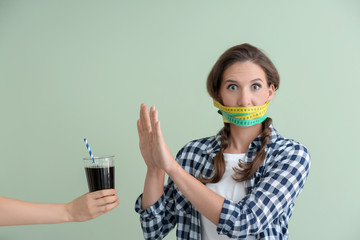 Woman with measuring tapes around her mouth refusing to drink unhealthy beverage on color...