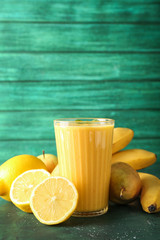 Glass of tasty yellow smoothie and fruits on color table